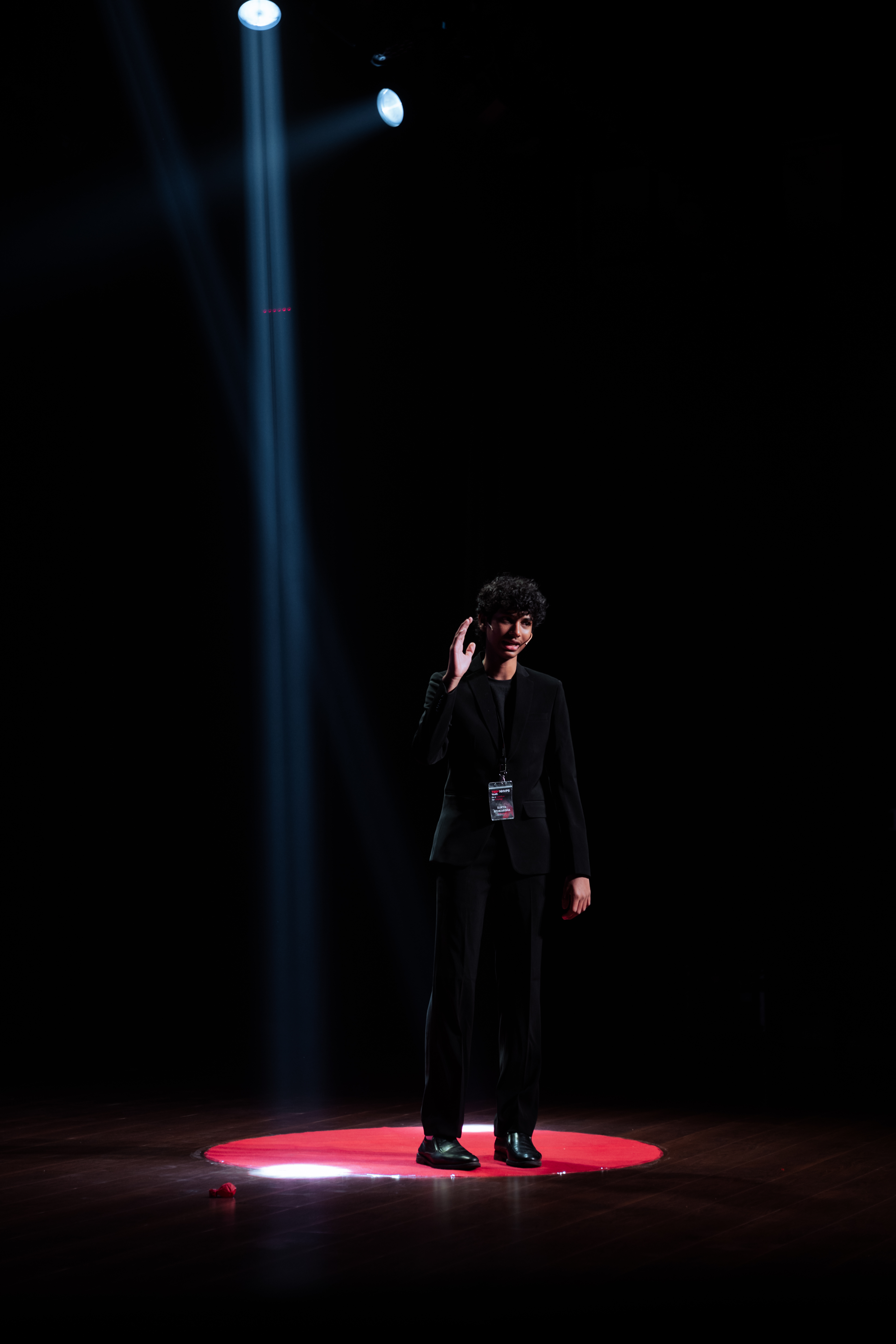 Surya Uthkarsha speaking on the TEDxNHVPS Youth stage under a spotlight
